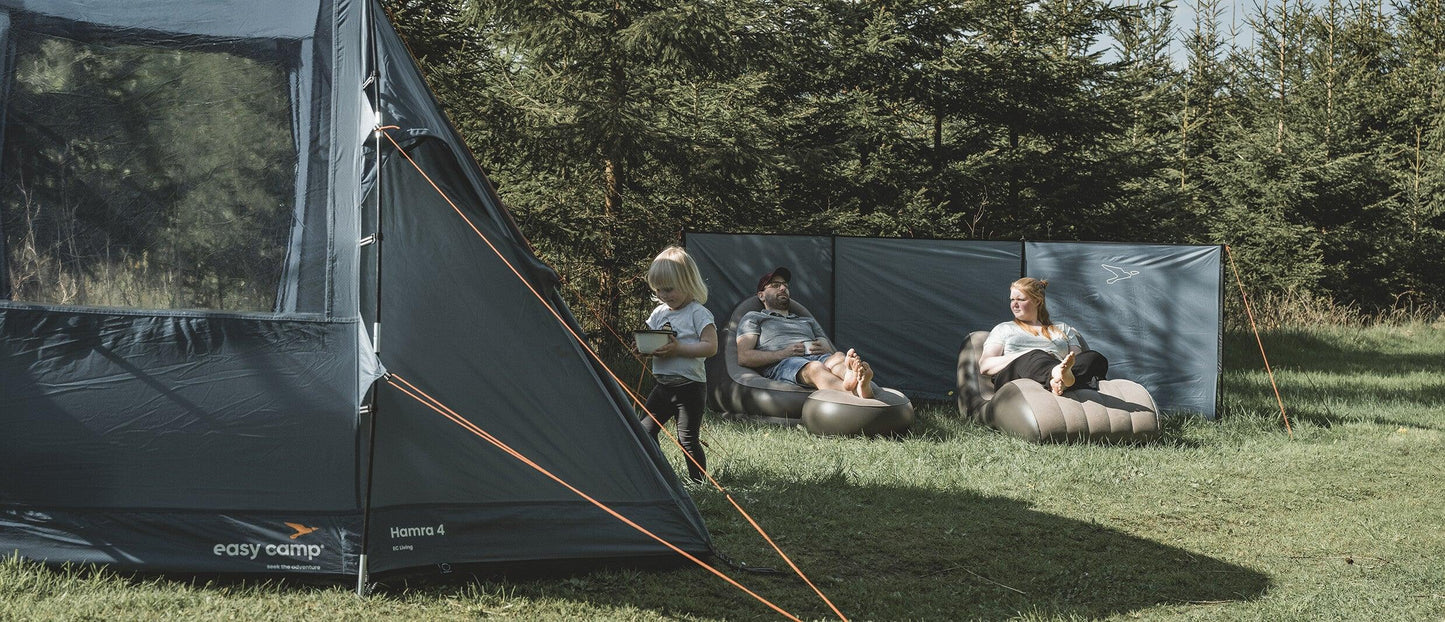 Family relaxing in camping chairs beside a tent in a forest setting, enjoying outdoor adventure gear.