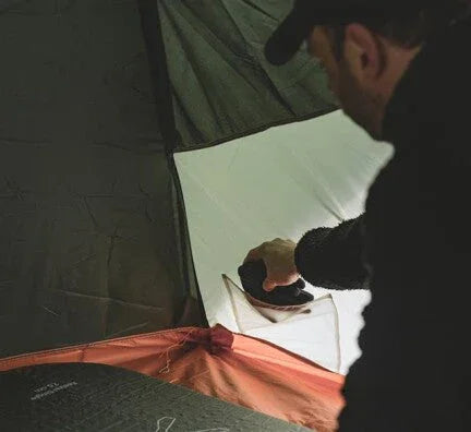 Man setting up camping tent with sleeping gear inside, perfect for outdoor adventures.