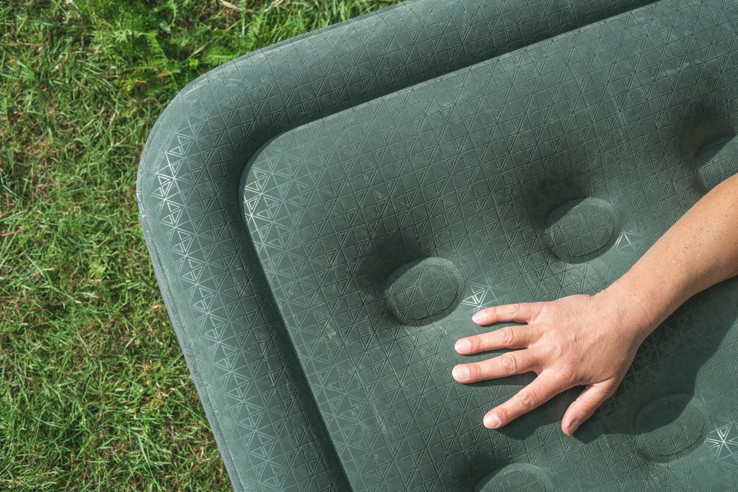 Green camping mattress with geometric pattern, hand pressing for comfort on grass