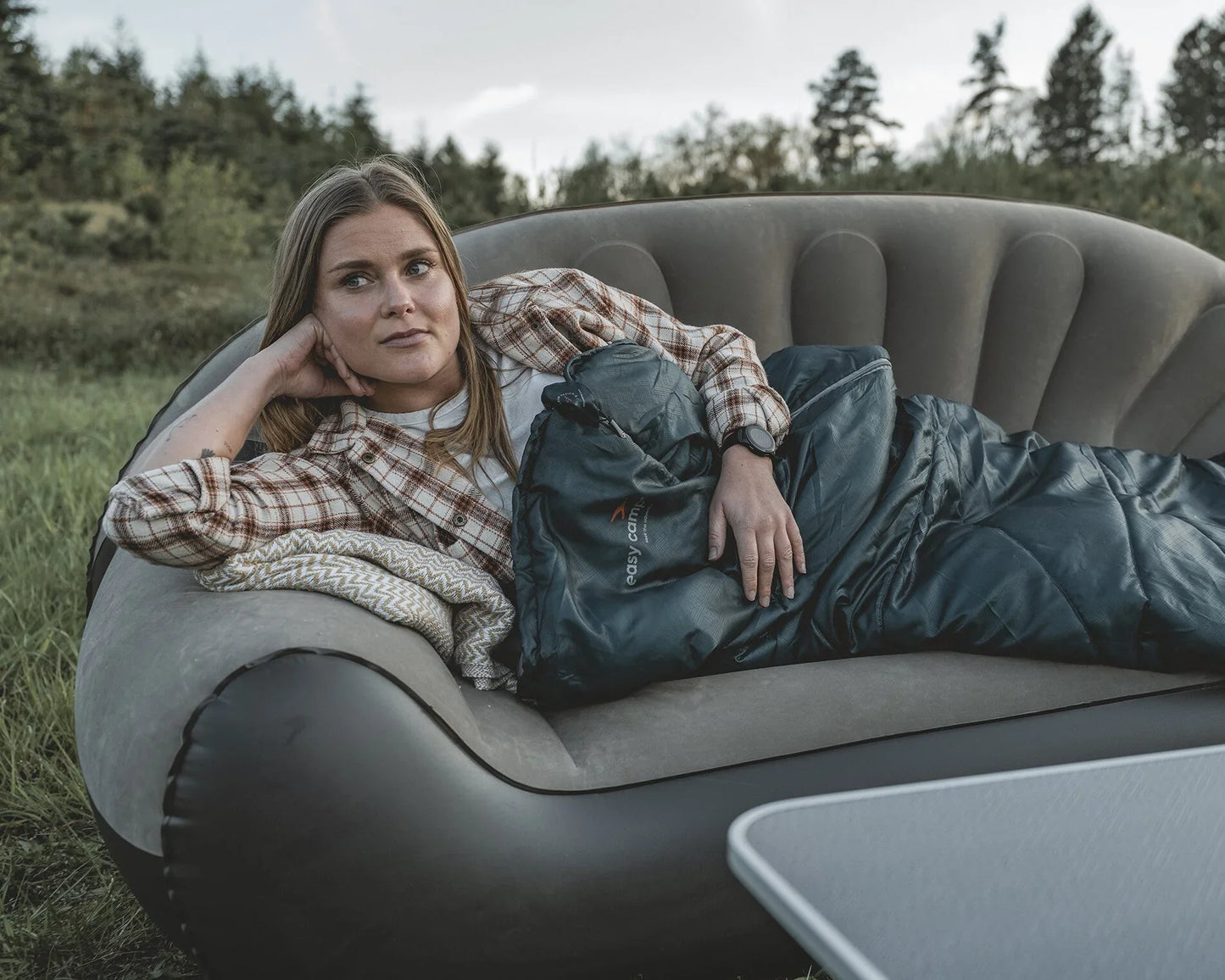 Woman relaxing in inflatable camping sofa with sleeping bag, outdoor gear for caravanning and camping adventures