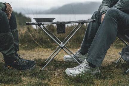 Portable camping table with cookware, set up outdoors near water for outdoor cooking adventures