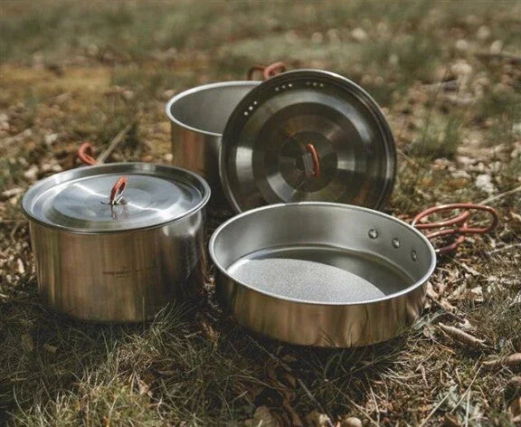 Stainless steel camping cookware set with lids on grass, ideal for outdoor adventures and caravanning.