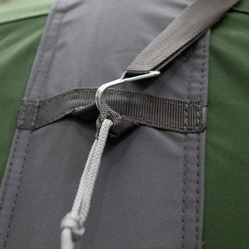 Close-up of a dark gray backpack strap with a silver metal carabiner and white rope, attached to a green backpack.
