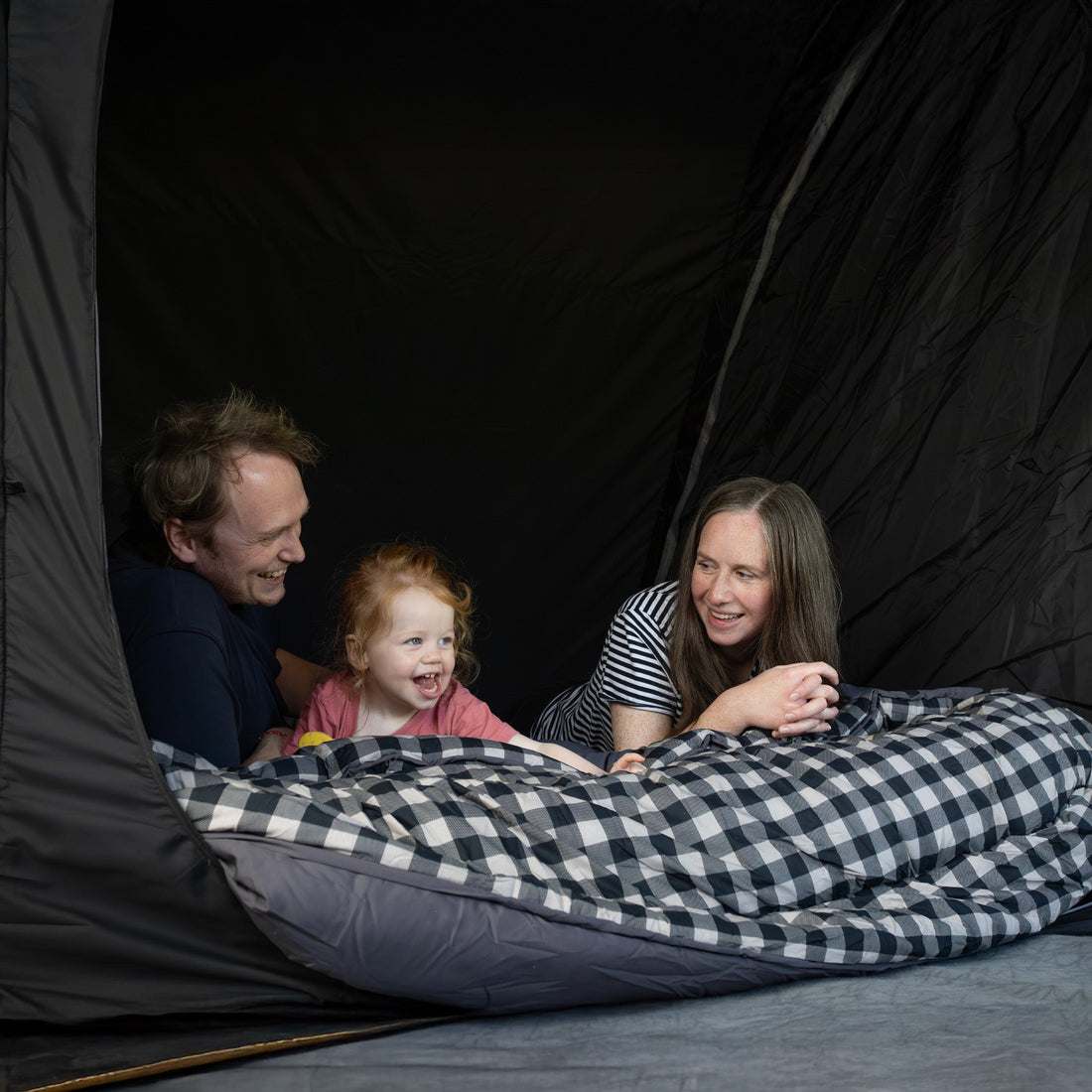 family looking out of a tent, on a checkered blanket