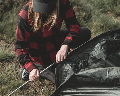 Person setting up a camping tent with poles in outdoor grassy area