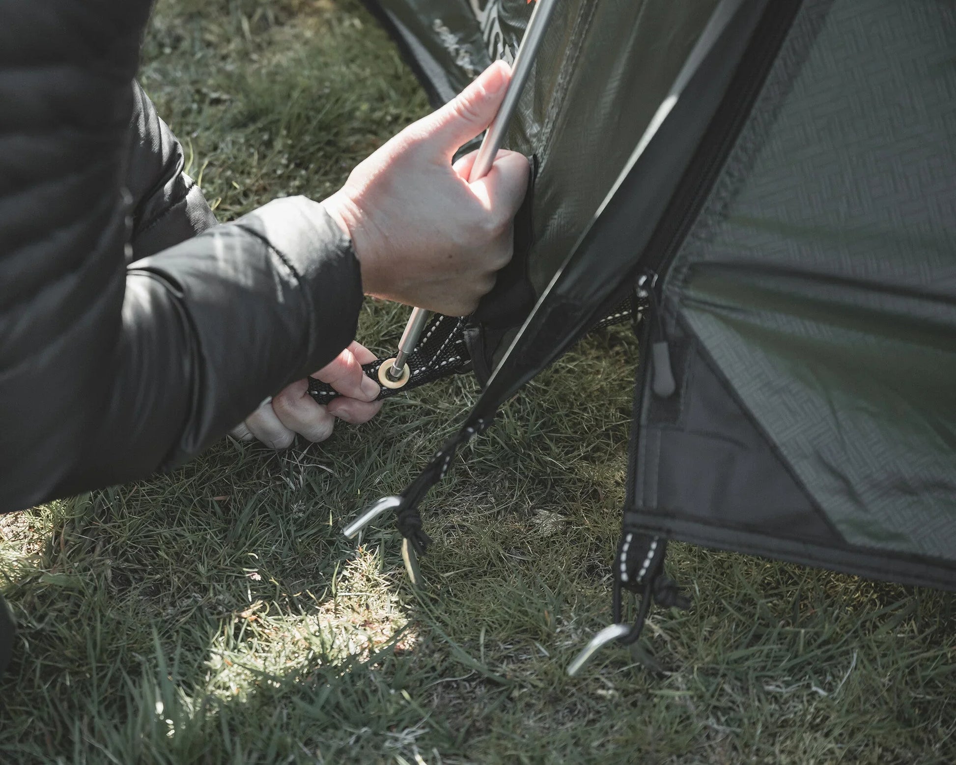 Setting up a camping tent with stakes on grassy ground