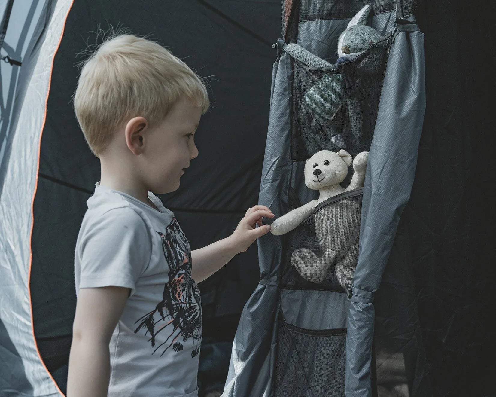 Child reaching for teddy bear in tent storage organizer, ideal for camping gear and kids' essentials