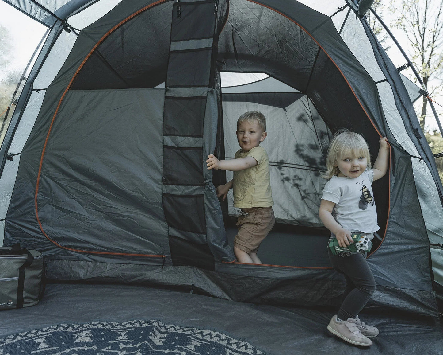 Two kids playing in a spacious family camping tent with mesh windows and orange trim, perfect for outdoor adventures.