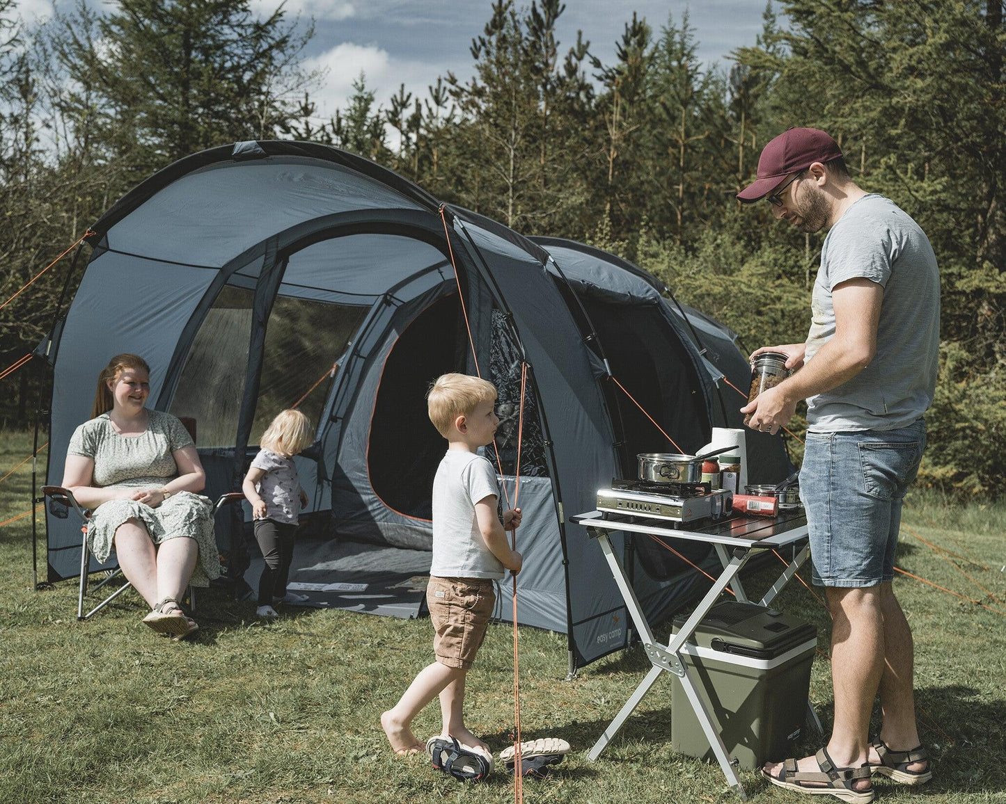 Family camping with tent, portable stove, and outdoor gear in forest setting