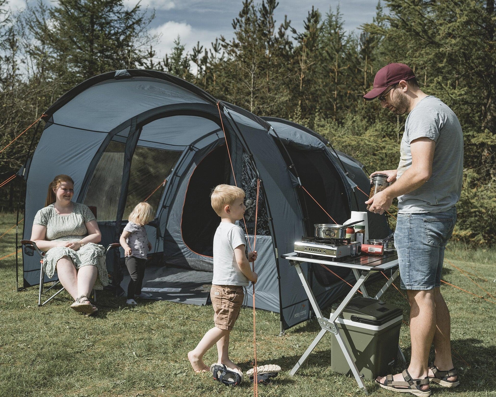 Family camping with tent, portable stove, and outdoor gear in forest setting