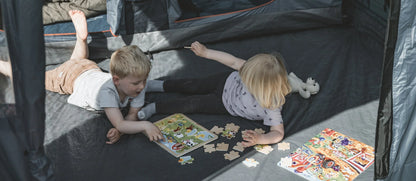Kids playing with puzzles inside a camping tent, enjoying outdoor family fun.