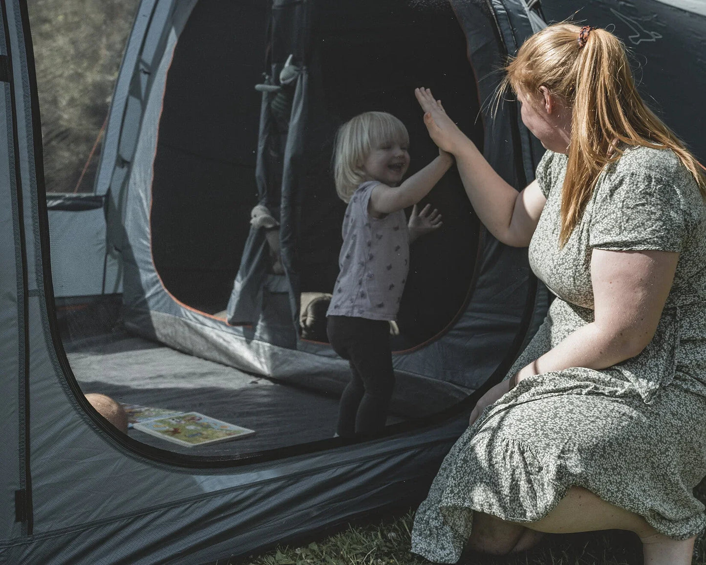 Mother and child high-fiving at camping tent entrance, enjoying outdoor family adventure