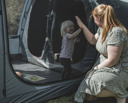 Mother and child high-fiving at camping tent entrance, enjoying outdoor family adventure