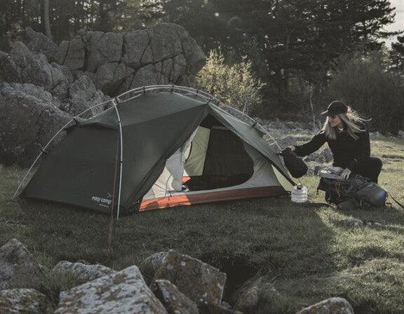 Camping tent setup in rocky outdoor setting with person preparing gear