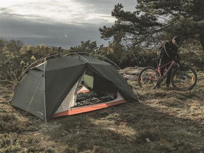 Green camping tent with orange trim set up outdoors near a cyclist with a mountain bike