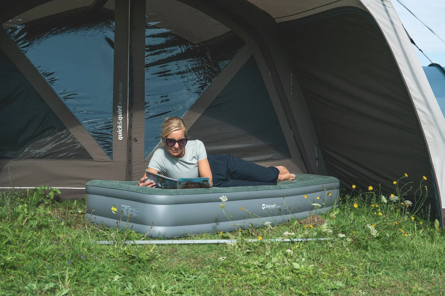 Woman relaxing on inflatable airbed inside tent, reading magazine during camping trip