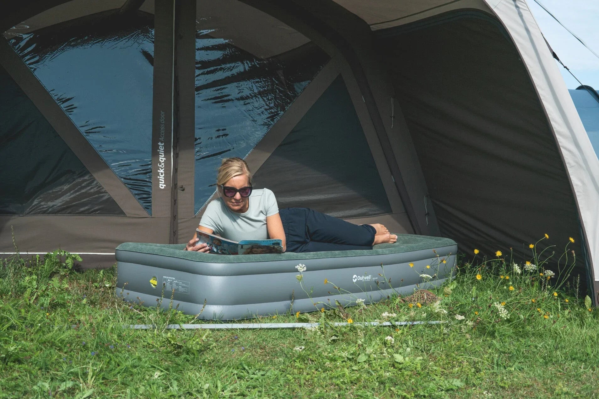 Woman relaxing on inflatable airbed inside tent, reading magazine during camping trip