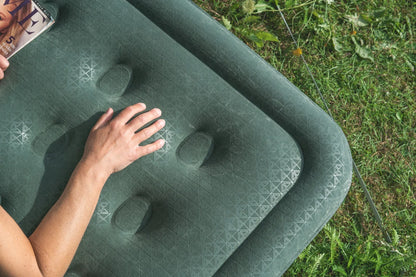 Green inflatable camping mattress with geometric pattern, hand resting on surface, grassy outdoor setting