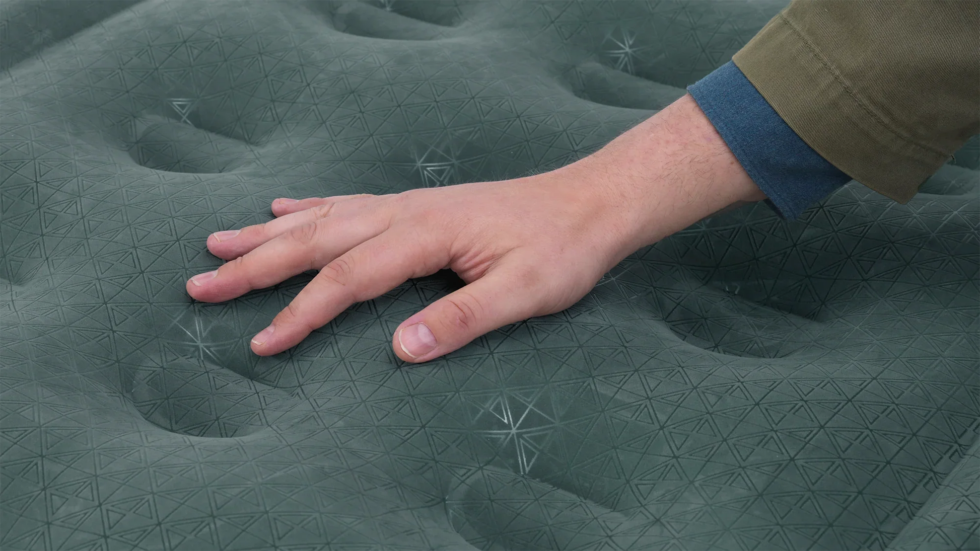 Hand pressing on green inflatable camping mattress with geometric texture for outdoor comfort
