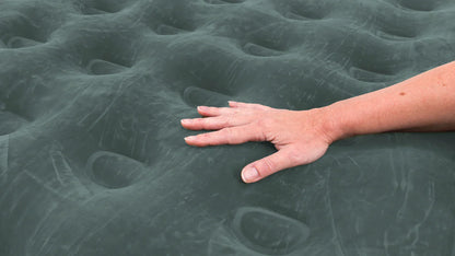 Hand pressing on dark green inflatable camping mattress showing comfort and support for outdoor sleeping gear