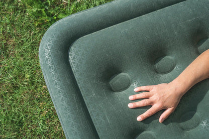 Green inflatable camping mattress with geometric texture, hand pressing on surface, on grass