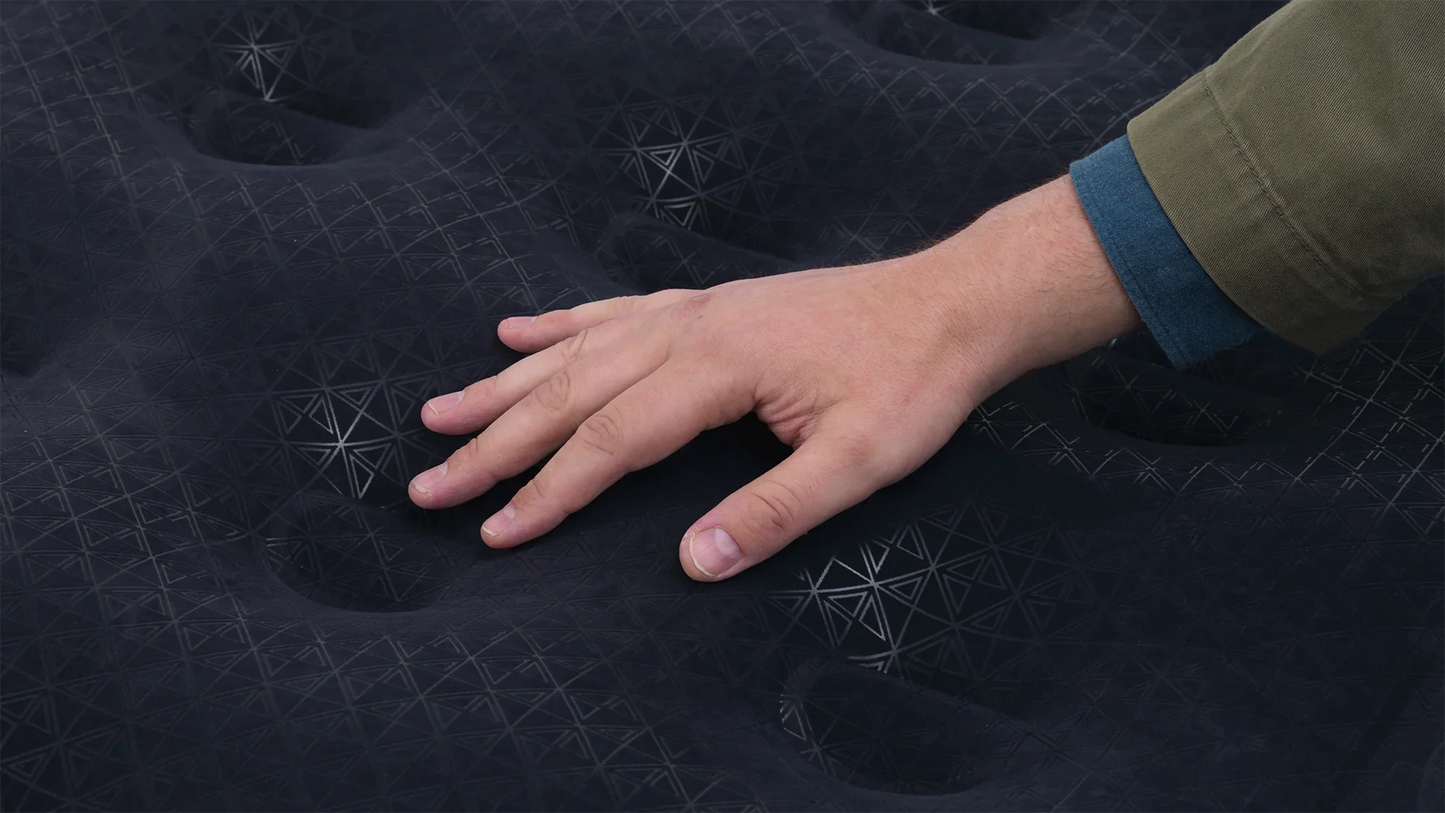 Hand pressing into black camping mattress with geometric pattern for outdoor comfort