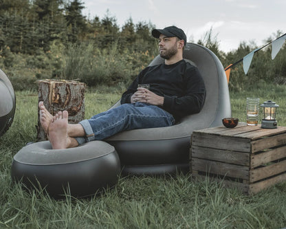 Man relaxing in grey inflatable camping chair with footrest outdoors, perfect for caravanning and camping adventures.