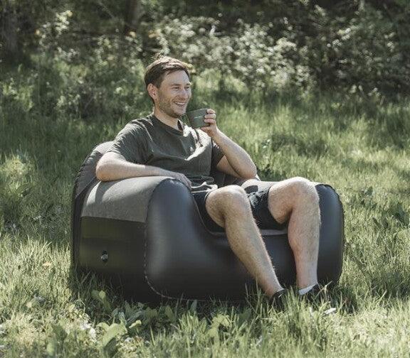 Man relaxing in inflatable camping chair outdoors with coffee, perfect for camping and caravanning adventures.
