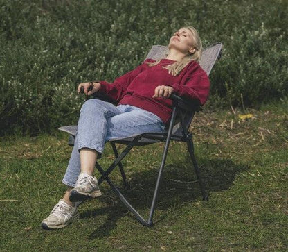 Woman relaxing in portable camping chair outdoors on grass, ideal for camping and outdoor adventures