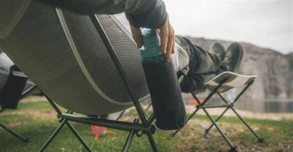 Camping chair with person relaxing outdoors, holding water bottle, ideal for caravanning and outdoor adventures.