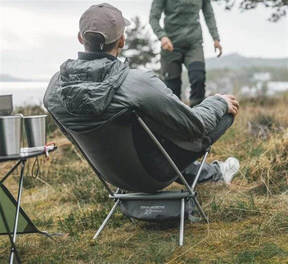 Man relaxing in portable camping chair outdoors near lakeside with cooking gear