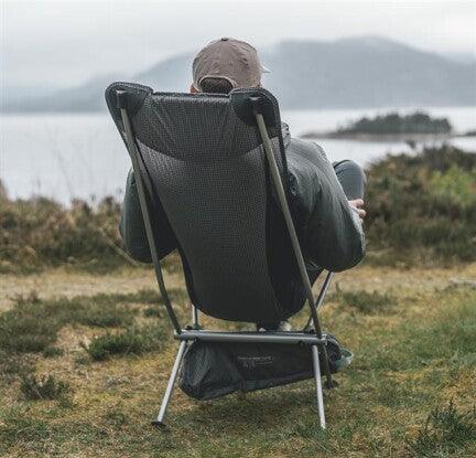 Portable camping chair with person relaxing outdoors near lakeside scenery