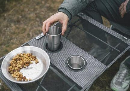 Camping table with stainless steel cups and snack bowl outdoors