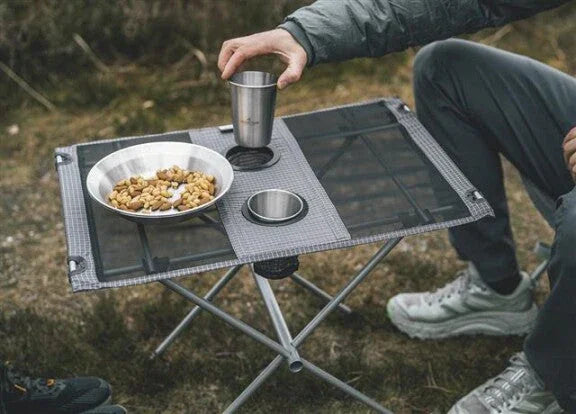 Portable camping table with metal bowls and cup, ideal for outdoor meals and caravanning adventures.