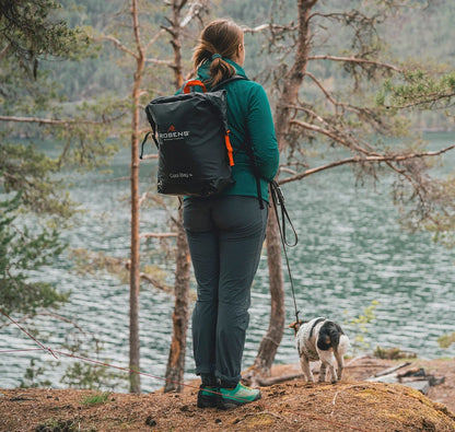 Woman hiking with dog near lake, wearing Robens backpack, outdoor adventure gear