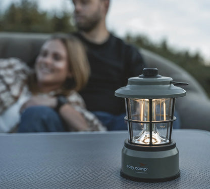 Easy Camp lantern illuminating outdoor table with couple relaxing in background