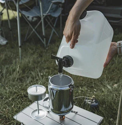 Pouring water into camping kettle on portable stove outdoors with folding chair nearby