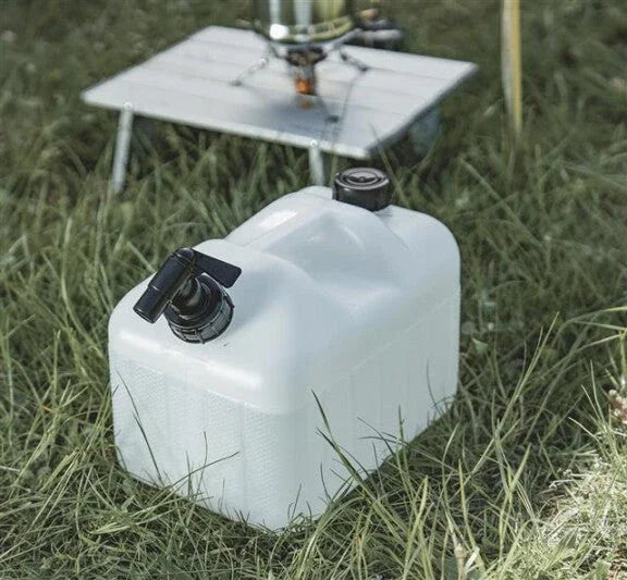 White portable water container with spigot for camping, placed on grass near outdoor cooking setup