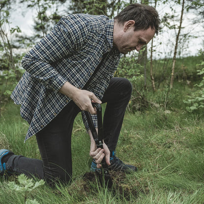 Man using camping shovel in grassy outdoor setting for outdoor adventures