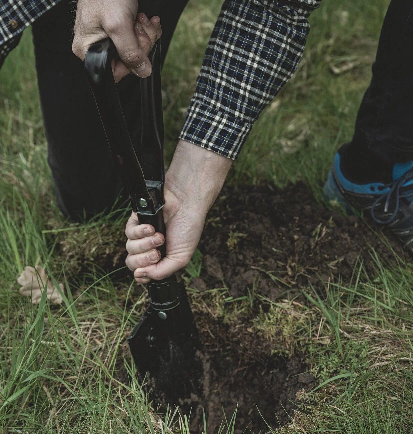 Person using camping shovel to dig in grassy outdoor setting