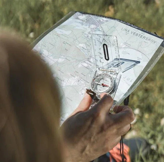 Hiker using compass and map for outdoor navigation during camping adventure