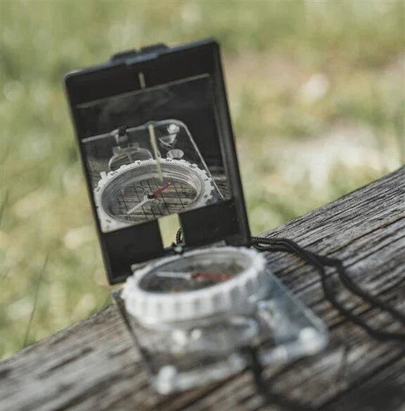 Portable compass for outdoor navigation on wooden surface, ideal for camping and hiking adventures.
