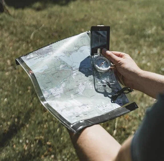 Person holding map and compass for outdoor navigation during camping or hiking adventures.
