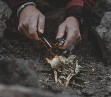Hands lighting a campfire with a lighter and kindling in outdoor setting
