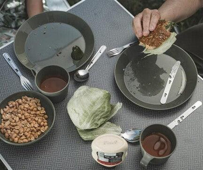 Outdoor camping meal setup with plates, utensils, and food on a portable table