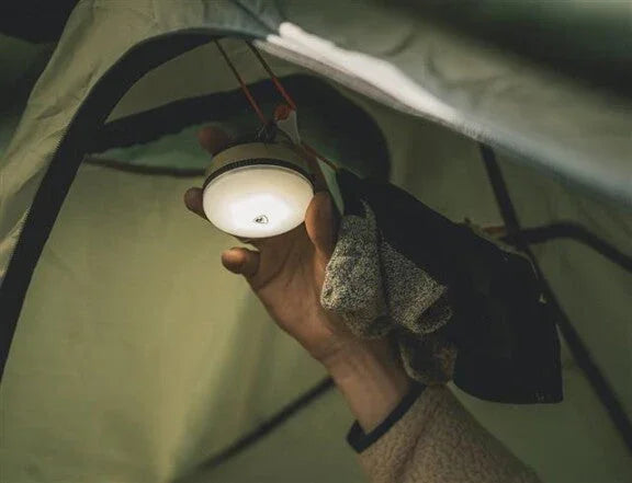 Hand holding portable camping lantern inside tent for outdoor adventures