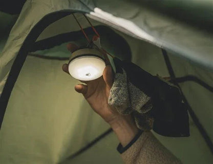 Hand holding portable camping lantern inside tent for outdoor adventures