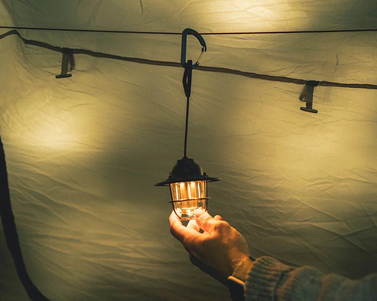 Portable camping lantern hanging inside tent, providing warm light for outdoor adventures