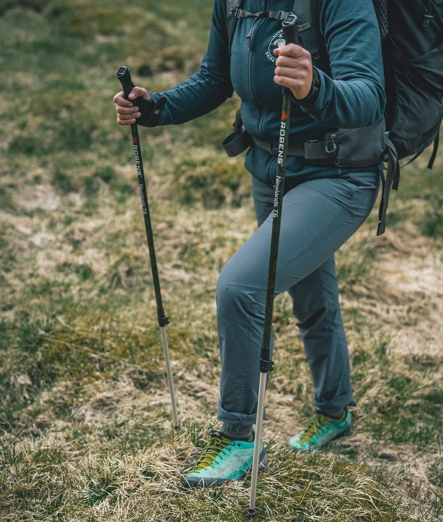 Hiker using Robens trekking poles on grassy trail with outdoor gear