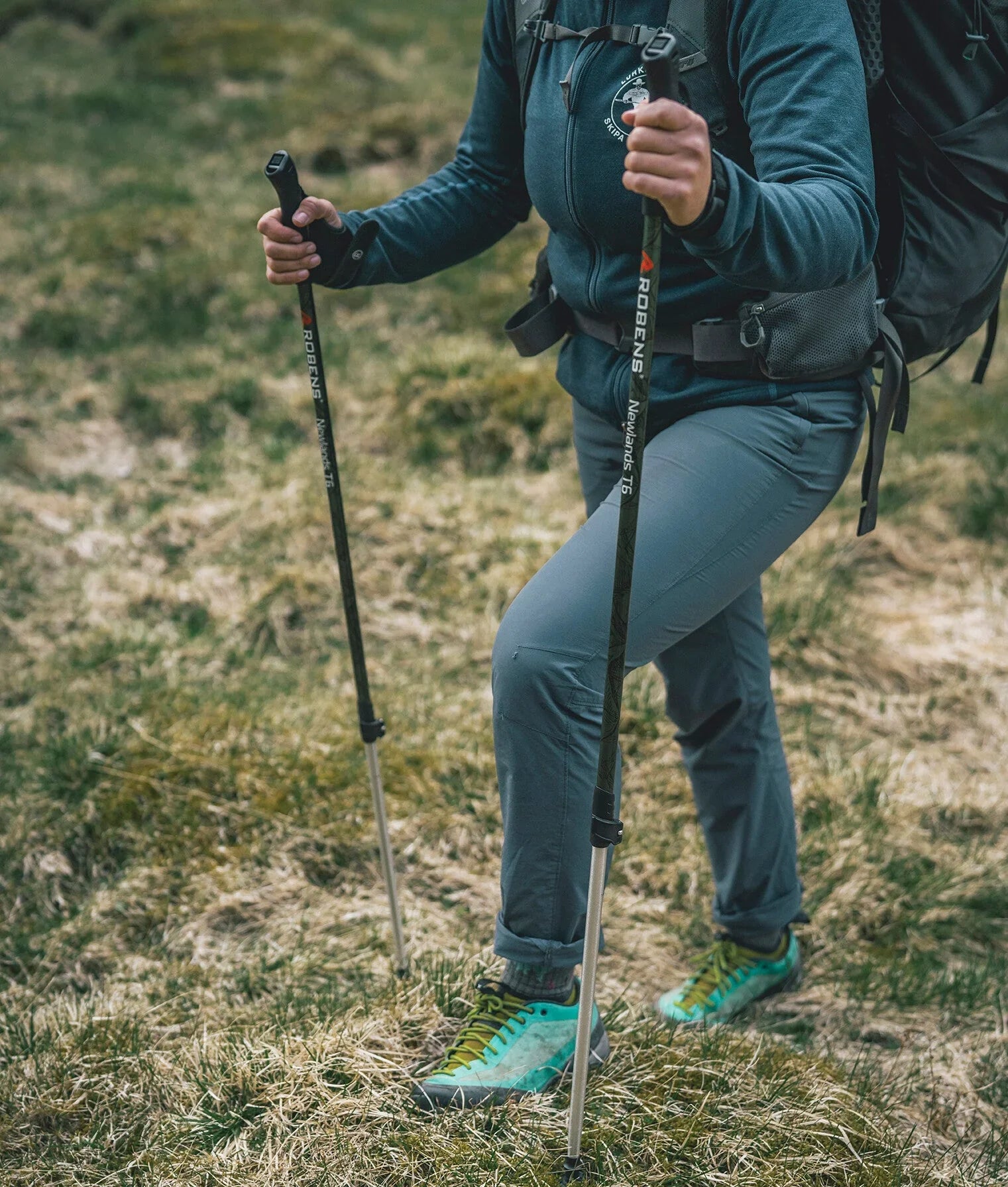 Hiker using Robens trekking poles on grassy trail with outdoor gear